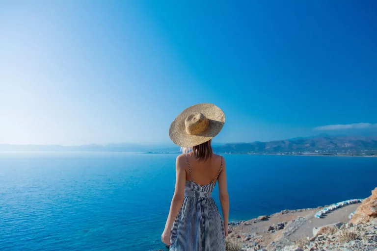 Jong roodharig meisje in hoed en jurk met zeekustlijn op Balos, Kreta, Griekenland