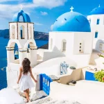 Santorini matkailu turisti nainen lomalla Oia kävely portaita. Henkilö valkoisessa mekossa vierailee kuuluisassa valkoisessa kylässä, jossa on Välimeri ja siniset kupolit. Euroopan kesäkohde.