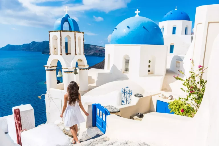 Voyage Santorini femme touristique en vacances à Oia marchant sur les escaliers. Personne en robe blanche visitant le célèbre village blanc avec la mer Méditerranée et les dômes bleus. Destination d'été en Europe.