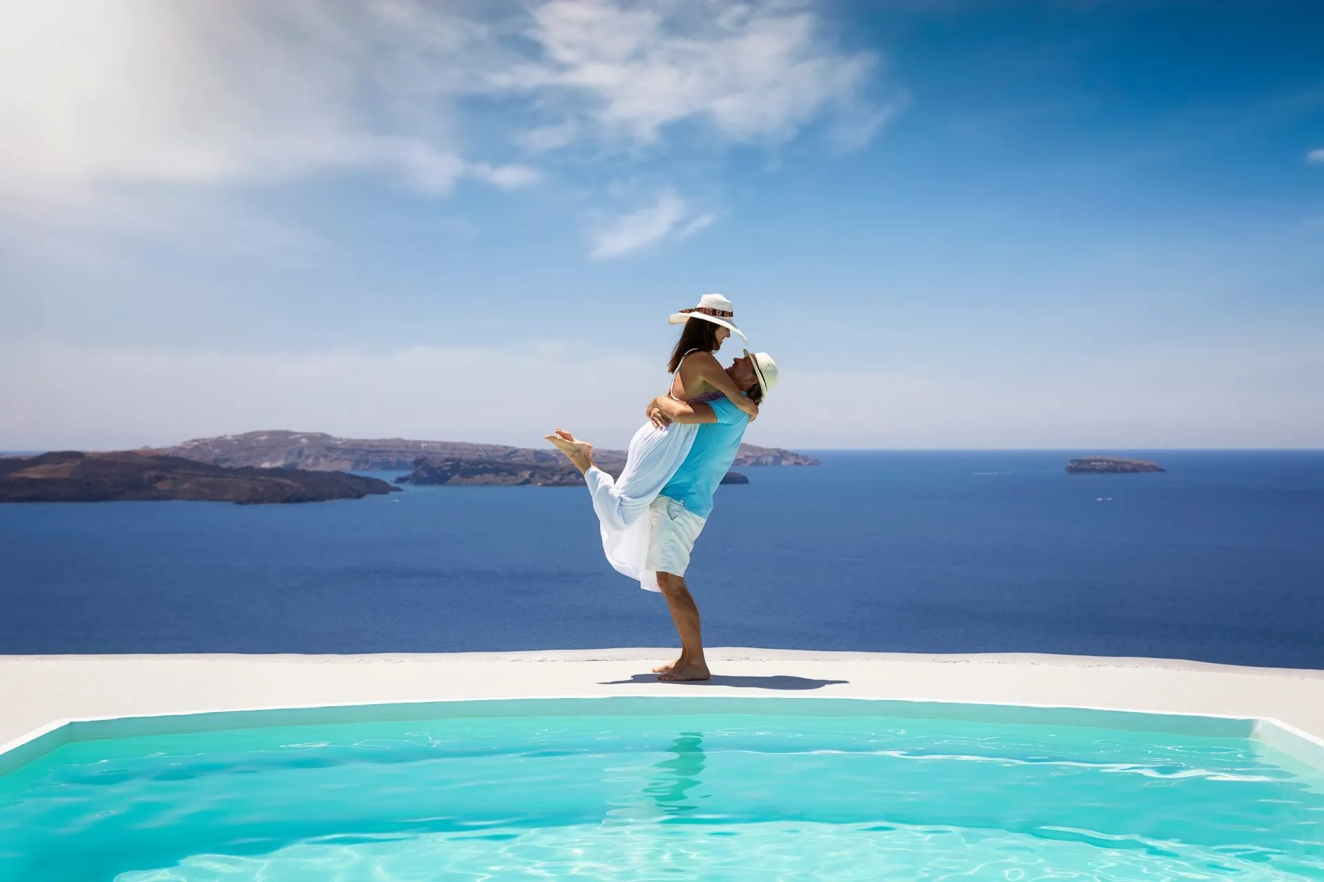 A happy summer holiday couple stands hugging a the swimming pool with view to the mediterranean sea